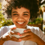 Close up of a woman with a cup of coffee sitting at cafe. African female having a coffee at outdoor coffeeshop.