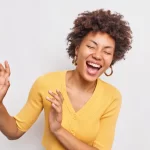 happy-overjoyed-curly-haired-afro-american-woman-dances-smiles-carefree-keeps-eyes-closed-dressed-casual-yellow-jumper-isolated-white-wall_273609-53280